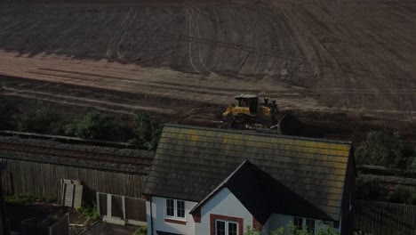 Aerial-view-following-Bulldozer-pushing-dirt-behind-housing-construction-site-in-the-early-morning-sunrise