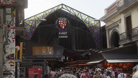 Entrada-Panorámica-Del-Famoso-Mercado-De-La-Boquería-En-Barcelona,-Peatones-Caminando-Por-La-Concurrida-Calle-Del-Mercado