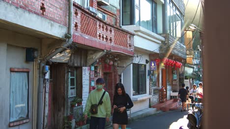 Young-couples-stroll-through-the-charming-narrow-streets,-exploring-the-sights-and-soaking-in-the-atmosphere-of-Jiufen's-historic-mountain-town,-static-shot-of-popular-tourist-attraction-in-Taiwan