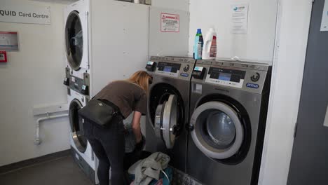 Woman-loads-clothes-into-washing-machines,-washing-center