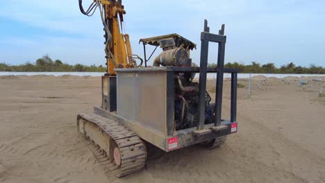 Trabajador-Operando-Una-Plataforma-De-Pilotaje-En-Un-Sitio-De-Construcción-De-Granja-Solar-Bajo-Cielos-Nublados,-Vista-Inclinada-Hacia-Abajo