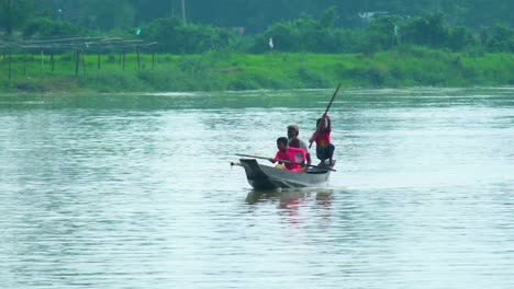 Two-kid-with-grandfather-paddling-a-boat-on-Surma-River-in-Sylhet,-Bangladesh