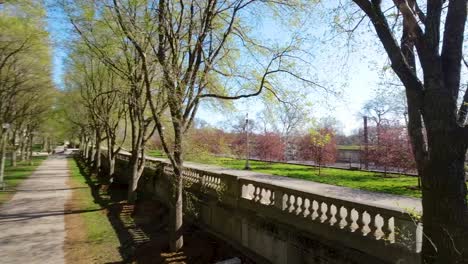 Imágenes-Aéreas-De-Drones-De-Una-Tranquila-Pasarela-Que-Serpentea-A-Través-De-Un-Exuberante-Parque-Verde-En-Chicago,-Flanqueada-Por-árboles-Y-Postes-De-Luz.