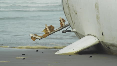 Waves-Rushing-Past-Washed-Up-Yacht-on-Gloomy-Beach---Keel-Close-Up-Shot