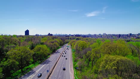 Rising-aerial-over-I-87-in-the-Bronx,-showcasing-a-clear-road,-green-parks,-and-NYC-skyline