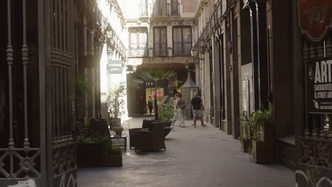 People-walking-around-the-narrow-city-streets-with-cafe's-and-restaurants-in-Barcelona,-Spain