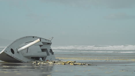 Wellen-Rauschen-An-Einer-Angeschwemmten-Yacht-Am-Düsteren-Strand-Vorbei---Weitwinkelaufnahme