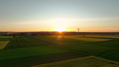 Vista-Aérea-De-Campos-Verdes-Y-Amarillos-Con-Una-Turbina-Eólica-Al-Atardecer