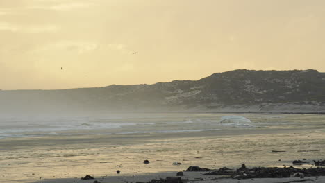 Sea-Water-Rushing-Past-Washed-Up-Yacht-on-a-Beach-During-Sunset