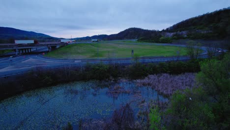 Toma-De-Drones-De-Una-Carretera-Y-Un-Humedal-Al-Atardecer,-Destacando-El-Tráfico-Tranquilo-Y-El-Paisaje-Natural.