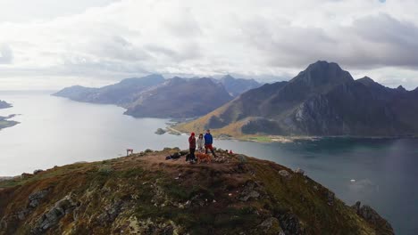 Aerial-360-orbit-around-a-couple-and-their-friend-at-the-peak-of-a-mountain-after-a-hike-in-the-Lofoten-Islands,-Norway