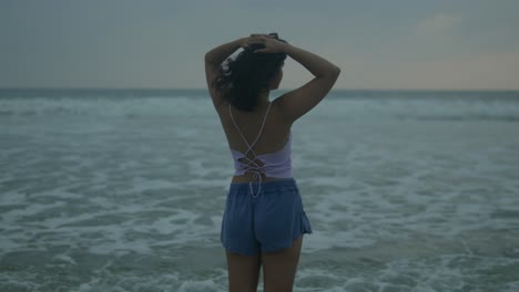 Frau-In-Sommerkleidung-Genießt-Ruhigen-Strand-In-Der-Abenddämmerung,-Haare-Zerzaust-Von-Sanfter-Brise