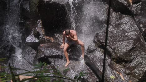 Ein-Mann-Posiert-Und-Lässt-Seine-Muskeln-Unter-Dem-Herabstürzenden-Wasser-Des-Kanto-Lampo-Wasserfalls-Auf-Bali-Spielen