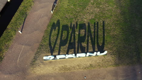 El-Cartel-&quot;I-Love-Pärnu&quot;-En-Forma-De-Corazón-Proyecta-Sombra-Sobre-El-Césped-En-Una-Vista-Aérea-De-Arriba-Hacia-Abajo