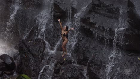 Una-Mujer-En-Bikini-Negro-Está-Parada-En-Las-Rocas-Bajo-El-Agua-De-La-Cascada-Kanto-Lampo-En-Bali.