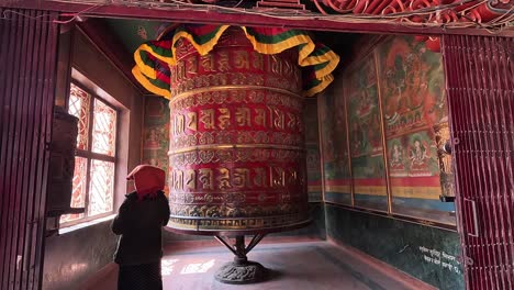Mujer-Girando-La-Ornamentada-Rueda-De-Oración-Dentro-Del-Monasterio-Guru-Lhakhang-En-Katmandú,-Girando-Silenciosamente-Mientras-Irradia-Energía-Espiritual-Y-Devoción