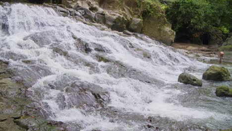 Woman-sits-in-waters-of-Goa-Rang-Reng-waterfall-on-Bali-island-in-Indonesia