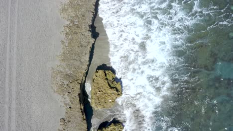 Von-Oben-Aufgenommene-Luftaufnahme-Einer-Drohne-Mit-Meereswellen,-Die-Auf-Felsen-Und-Strand-Krachen,-Florida