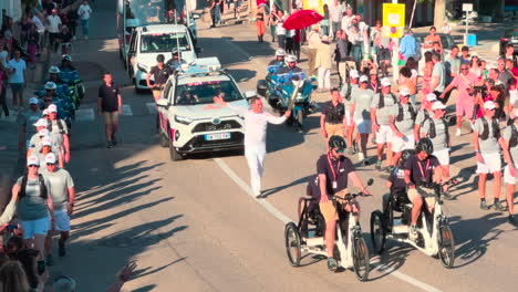 Relevo-De-La-Antorcha-Olímpica-En-Toulon,-Gente-Animando-Y-Escoltando-Al-Portador-De-La-Antorcha-En-Un-Día-Soleado