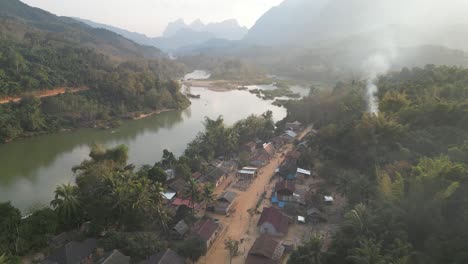 drone-shot-of-smoke-rising-from-remote-village-in-the-mountain-town-of-Nong-Khiaw-in-Laos,-Southeast-Asia
