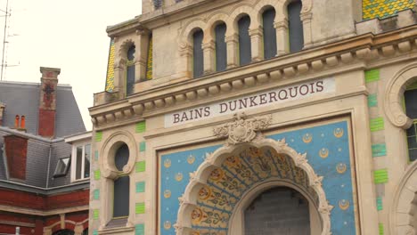 Historic-Bains-Dunkerquois-in-Dunkerque,-France-showcasing-intricate-blue-and-gold-facade-under-overcast-sky