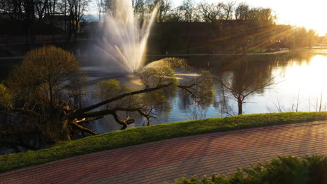 Dzirnavu-Teich-Mit-Springbrunnen-Mit-Magischen-Sonnenstrahlen,-Seitliche-Luftaufnahme