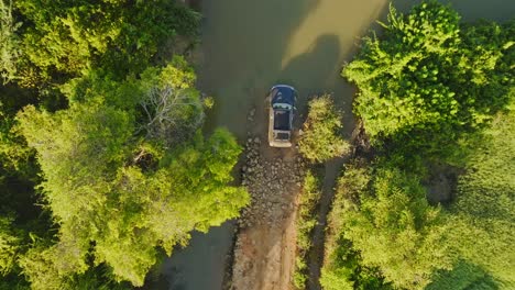 Aerial-top-down-view-on-black-SUV-Off-Road-Vehicle-on-a-green-forest-road-passing-through-deep-mud-puddle-on-sunny-day-in-Africa
