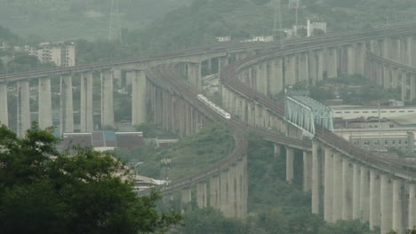 Looking-down-from-the-mountaintop,-high-speed-trains-are-running-in-the-city