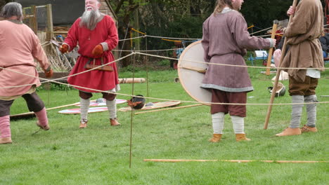 medieval-reenactment,-individuals-in-authentic-costumes-showcase-a-sword-battle,-set-against-a-backdrop-of-wooden-structures-and-greenery,-capturing-the-essence-of-historical-combat