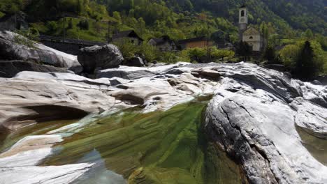 Pan-up-from-cool-green-water-pool-to-chapel-in-Verzasca-Lavertezzo-Switzerland