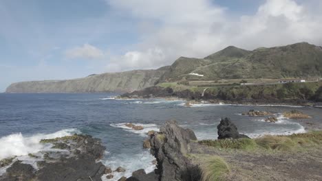 Waves-crash-against-rocky-shore-in-Mosteiros,-Sao-Miguel-with-a-clear-sky-and-distant-cliffs