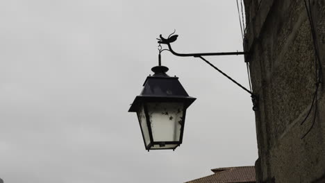 Old-style-lantern-with-bugs-inside-hangs-off-thin-metal-frame-from-stone-wall