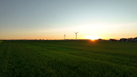 Expansive-green-fields-with-wind-turbines-at-sunset,-distant-houses,-golden-light,-tranquil