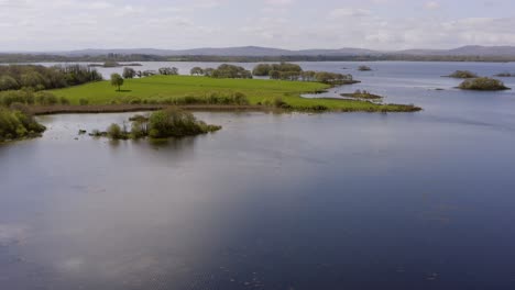 Drone-pullback-flies-over-lake-below-castle-on-hillside-forest,-Ireland