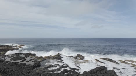 Coastal-view-of-Mosteiros,-Sao-Miguel-with-crashing-waves-and-lush-cliffs-under-a-blue-sky