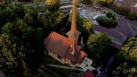 4K-Filmmaterial-Einer-Drohne,-Die-Auf-Eine-Holzkirche-Herabfliegt-Und-Einen-Atemberaubenden-Blick-Auf-Die-Gebäude-Bietet,-Die-Vom-Sonnenuntergang-Beleuchtet-Werden