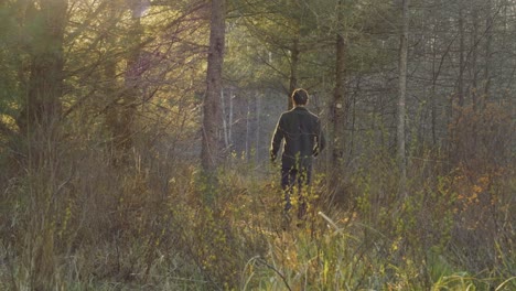 Man-walking-through-a-forest-with-sunlight-filtering-through-the-trees,-surrounded-by-nature-and-lush-vegetation