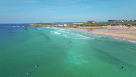 Playa-Fistral-En-Newquay-Con-Surfistas,-Aguas-Turquesas-Y-Una-Costa-Pintoresca-Con-El-Hotel-Headland-Al-Fondo