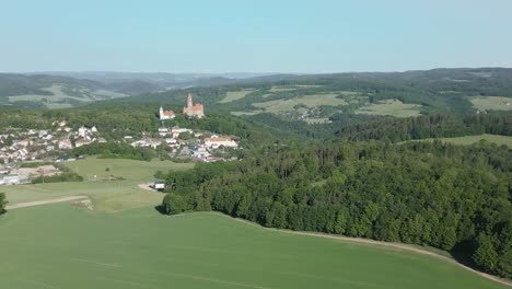 Aerial-view-of-majestic-Bouzov-Castle-in-the-Czech-Republic,-perched-atop-a-hill-and-surrounded-by-verdant-forests-and-a-quaint-village