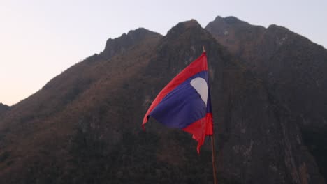 Laos-flag-flapping-in-the-wind-in-the-mountain-town-of-Nong-Khiaw-in-Laos,-Southeast-Asia