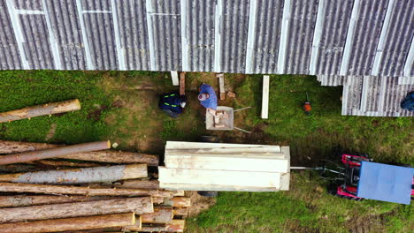 Two-workers-preparing-workplace-for-a-wooden-plank-pile,-aerial-top-down-view