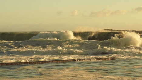 Rough-Sea-Waves-Crashing-On-Rocky-Shoreline-Creating-Huge-Spray-During-Golden-Sunset---Wide-Pan-Shot