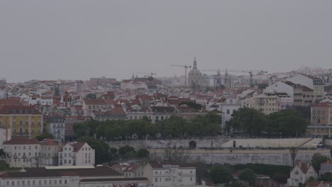 View-of-The-Royal-Basilica-of-Estrela-with-cranes-surrounding-it-and-beautiful-Lisbon-cityscape-in-Lisbon,-Portugal