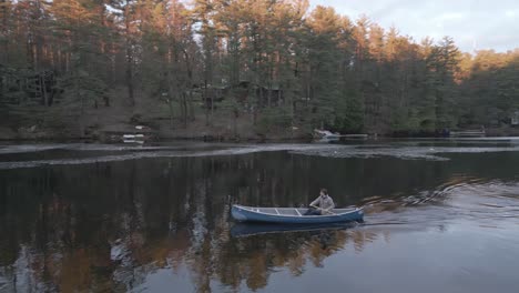 Person-paddling-a-canoe-on-a-tranquil-river-surrounded-by-forested-banks-at-sunrise,-with-calm-water-reflecting-the-trees