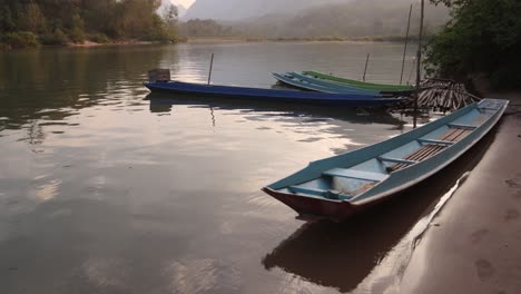 Barcos-De-Madera-Atracados-En-La-Orilla-Del-Río-En-La-Ciudad-Montañosa-De-Nong-Khiaw-En-Laos,-Sudeste-De-Asia