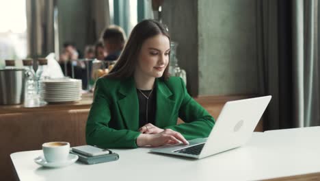 Una-Mujer-Encantadora-Con-Una-Chaqueta-Verde-Comienza-A-Bailar-Mientras-Está-Sentada-En-Una-Mesa-En-Un-Restaurante-Con-Buen-Humor-Y-Una-Sonrisa.