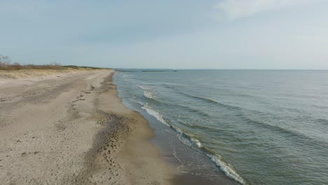 Aerial-establishing-view-of-sea-waves-crashing-into-the-beach-with-white-sand-on-a-sunny-spring-day,-Baltic-sea,-Pape-beach,-Latvia,-ascending-wide-angle-drone-shot-moving-forward
