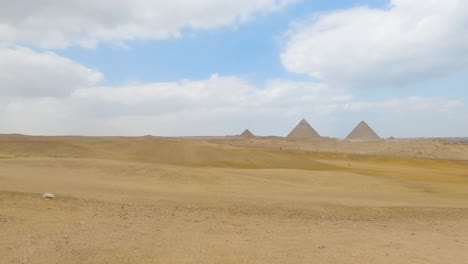 Pan-across-sand-desert-dunes-to-view-of-three-pyramids-off-in-the-distance