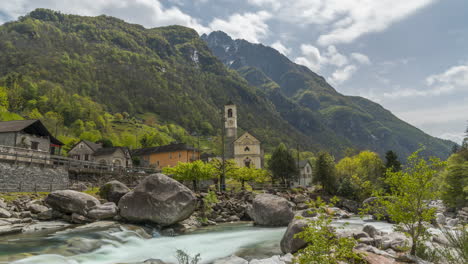 Wolkenschatten-Ziehen-über-Einen-Lebendigen-Frühlingsberg-über-Einer-Kirche-Und-Einem-Felsigen-Bach-In-Lavertezzo,-Schweiz