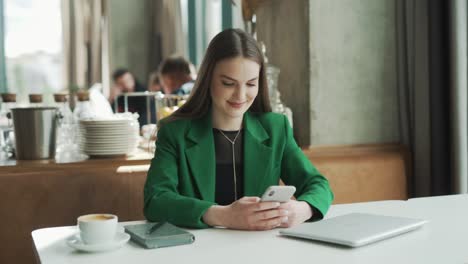 Junge-Professionelle-Kaukasische-Frau-Mit-Einem-Smartphone-Lächelt-In-Einem-Restaurant